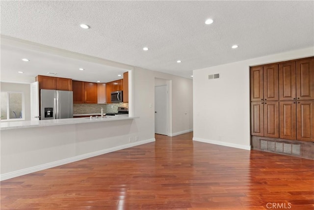 kitchen featuring a textured ceiling, wood-type flooring, stainless steel appliances, sink, and backsplash