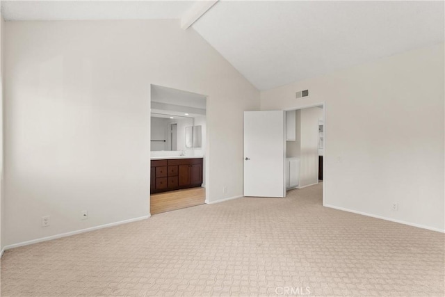 unfurnished bedroom featuring ensuite bathroom, beamed ceiling, light colored carpet, high vaulted ceiling, and sink