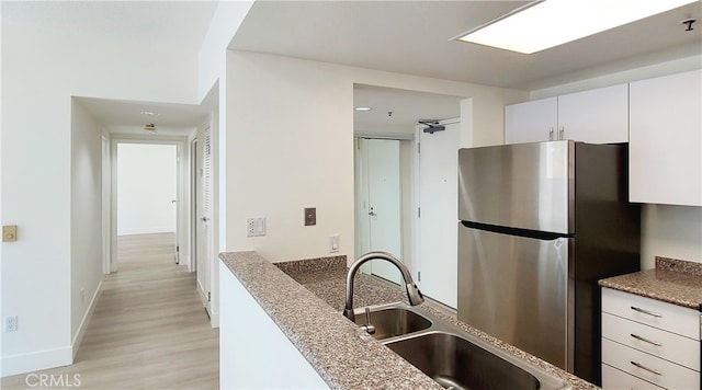 kitchen featuring white cabinetry, stainless steel refrigerator, light hardwood / wood-style flooring, light stone counters, and sink