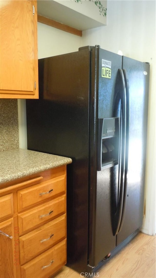 kitchen featuring backsplash, black refrigerator with ice dispenser, and light wood-type flooring