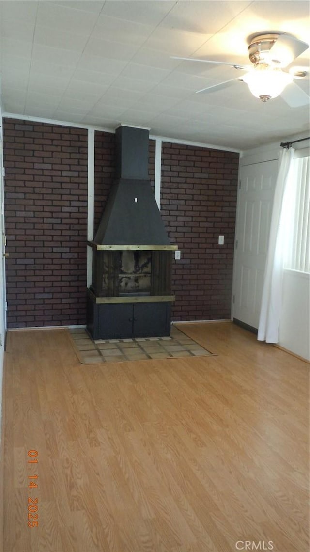 unfurnished living room featuring hardwood / wood-style floors, a wood stove, and brick wall