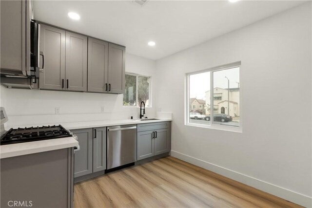 kitchen with gas stove, gray cabinets, stainless steel dishwasher, sink, and light wood-type flooring