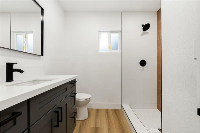 bathroom featuring wood-type flooring, toilet, vanity, and a tile shower