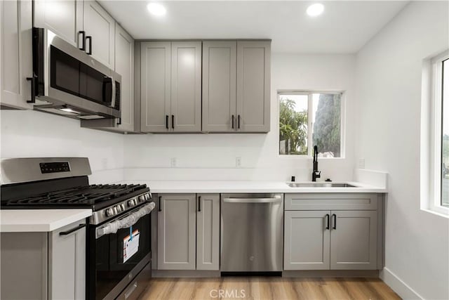 kitchen with sink, appliances with stainless steel finishes, gray cabinets, and light hardwood / wood-style flooring