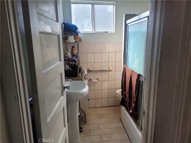 bathroom featuring toilet, enclosed tub / shower combo, and tile walls