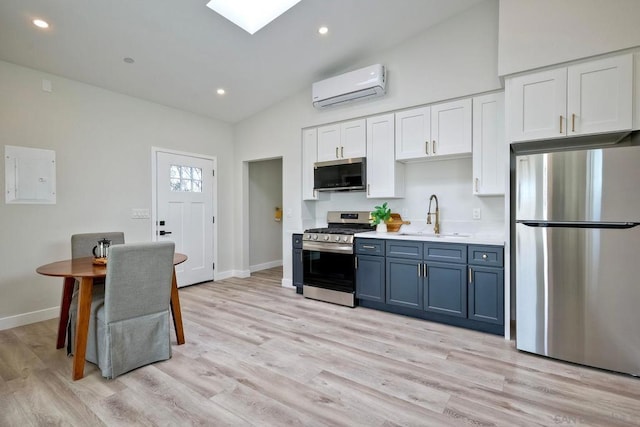 kitchen featuring lofted ceiling with skylight, sink, a wall mounted air conditioner, stainless steel appliances, and white cabinets