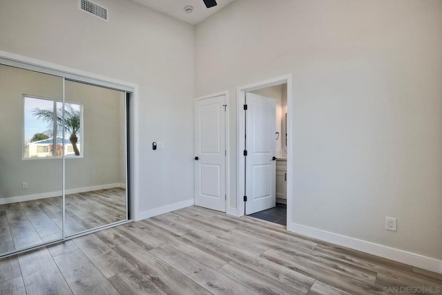 unfurnished bedroom with light wood-type flooring, a closet, ensuite bathroom, and a high ceiling