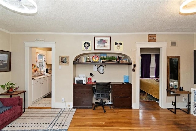 office area with crown molding, light hardwood / wood-style floors, sink, and a textured ceiling