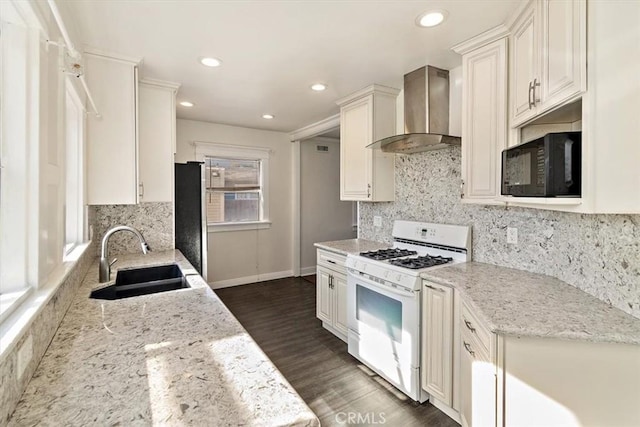 kitchen featuring wall chimney range hood, sink, stainless steel refrigerator, light stone countertops, and white gas range