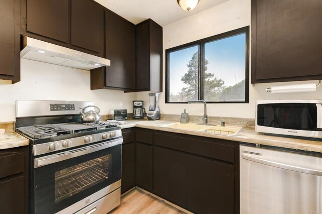 kitchen featuring sink, appliances with stainless steel finishes, dark brown cabinets, and light wood-type flooring