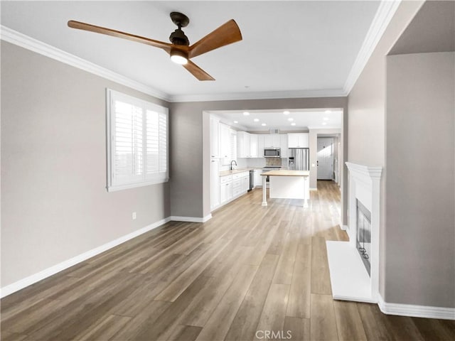 unfurnished living room featuring ceiling fan, sink, crown molding, and light hardwood / wood-style floors