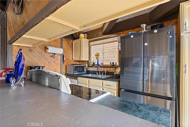 kitchen featuring appliances with stainless steel finishes, cream cabinetry, wood walls, and sink