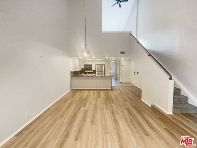 unfurnished living room featuring light wood-type flooring, ceiling fan, and a towering ceiling