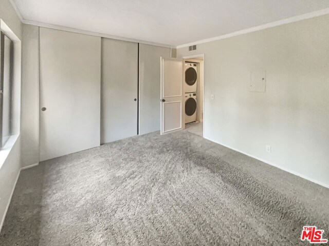 unfurnished bedroom featuring stacked washing maching and dryer, a closet, carpet flooring, and crown molding