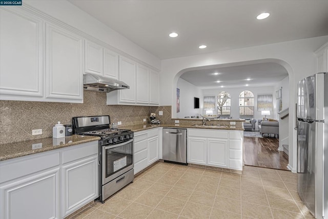 kitchen featuring kitchen peninsula, appliances with stainless steel finishes, light tile patterned floors, stone counters, and white cabinets