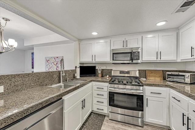 kitchen featuring white cabinetry, stainless steel appliances, an inviting chandelier, light hardwood / wood-style floors, and sink