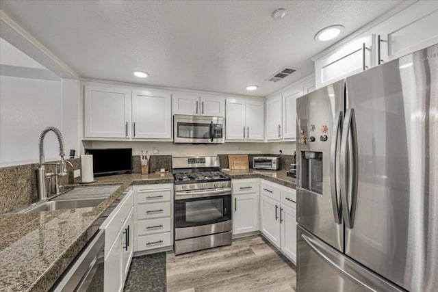 kitchen featuring sink, white cabinetry, light hardwood / wood-style flooring, stainless steel appliances, and dark stone counters