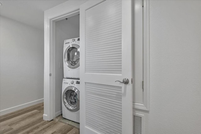 washroom with stacked washing maching and dryer and light hardwood / wood-style floors