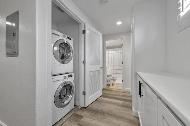 clothes washing area featuring electric panel, light hardwood / wood-style flooring, and stacked washing maching and dryer