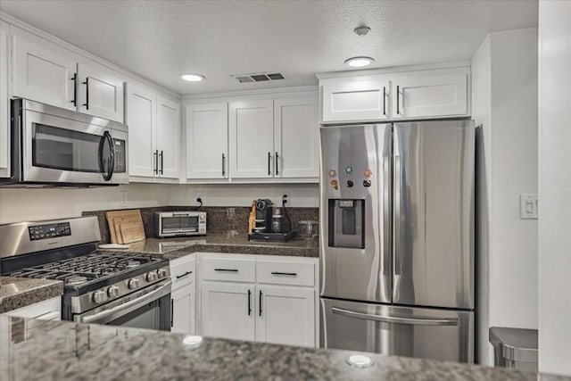 kitchen featuring stainless steel appliances, dark stone countertops, and white cabinets