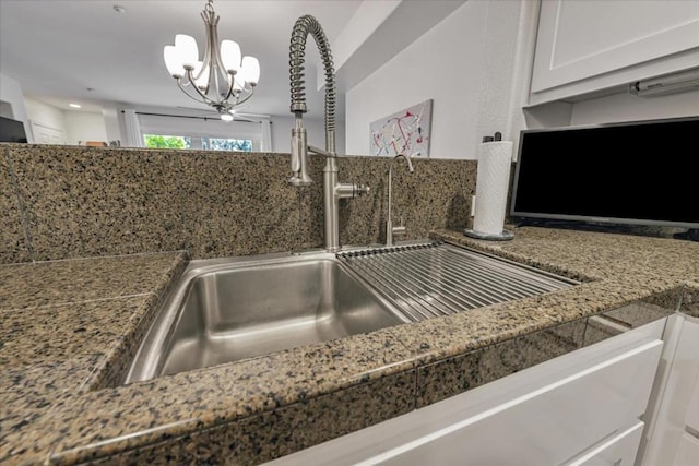 details with decorative light fixtures, white cabinets, sink, and a chandelier