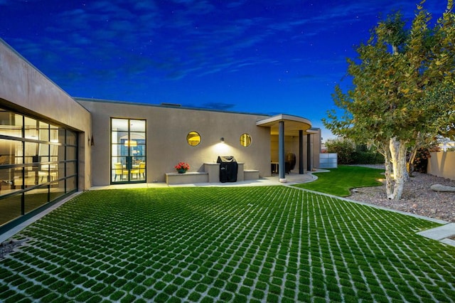 back house at dusk featuring a lawn