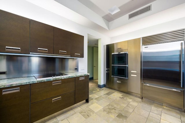 kitchen featuring light stone countertops, dark brown cabinetry, stainless steel built in refrigerator, black electric stovetop, and double oven