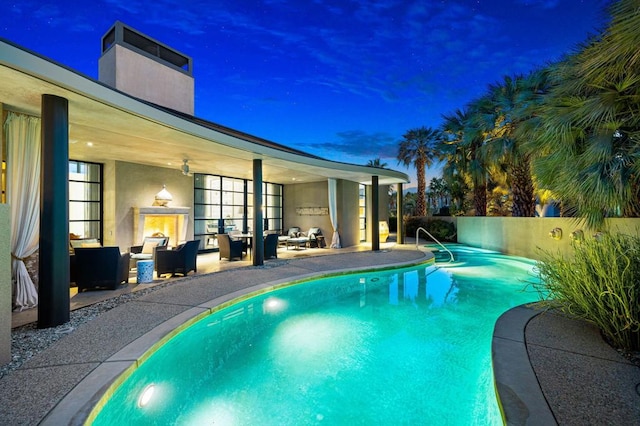 pool at dusk with an outdoor living space with a fireplace and a patio