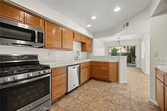 kitchen with pendant lighting, kitchen peninsula, sink, stainless steel appliances, and light tile patterned floors