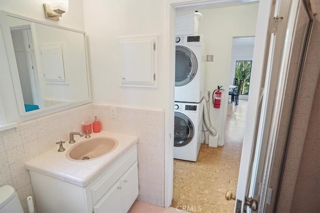 bathroom with toilet, vanity, stacked washer and dryer, and tile walls