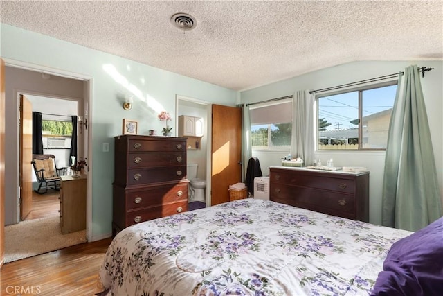 bedroom with a textured ceiling, light wood-type flooring, connected bathroom, and vaulted ceiling