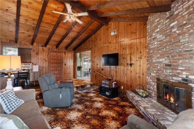 living room featuring wood ceiling, wood walls, a brick fireplace, ceiling fan, and beamed ceiling