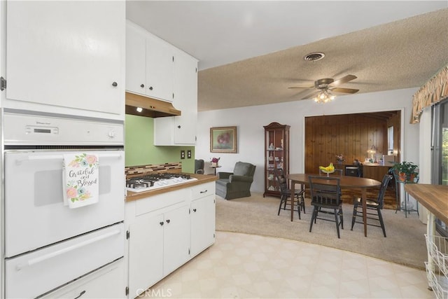 kitchen with white appliances, white cabinets, a textured ceiling, light carpet, and ceiling fan