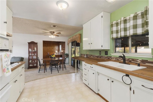 kitchen with a healthy amount of sunlight, wooden counters, sink, and white cabinetry