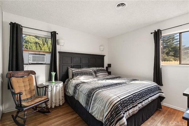 bedroom with cooling unit, dark wood-type flooring, multiple windows, and a textured ceiling