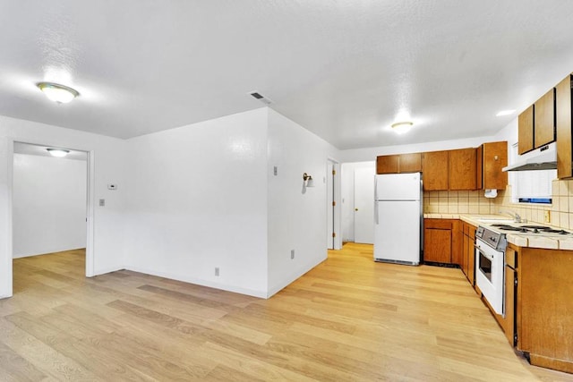 kitchen with white appliances, sink, light hardwood / wood-style floors, and decorative backsplash