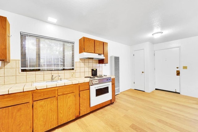 kitchen with sink, tile countertops, electric range, and light hardwood / wood-style flooring