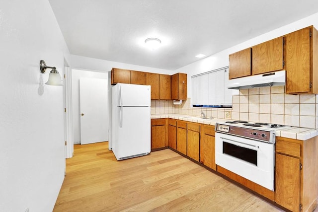 kitchen with sink, light wood-type flooring, tile counters, white appliances, and decorative backsplash