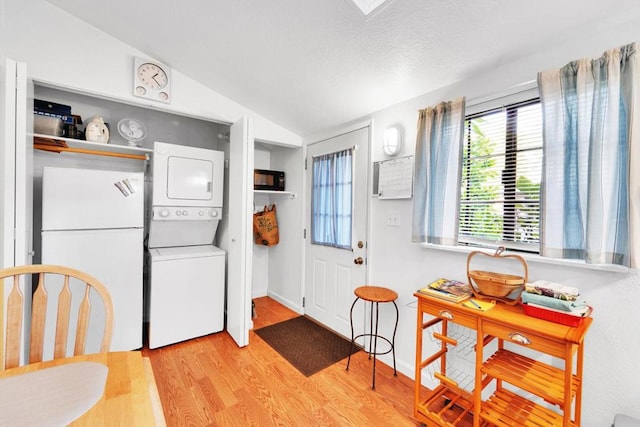 kitchen with stacked washer / drying machine, light hardwood / wood-style flooring, vaulted ceiling, and white fridge