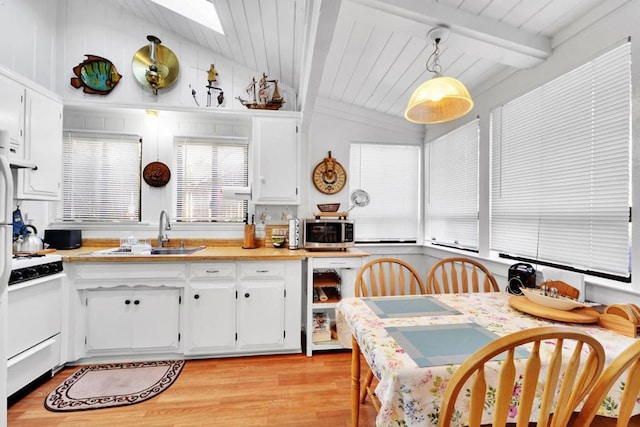 kitchen featuring sink, white cabinetry, vaulted ceiling with skylight, white range, and decorative light fixtures