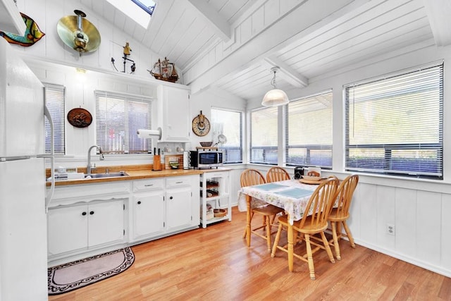 kitchen with hanging light fixtures, white cabinetry, white fridge, and lofted ceiling with skylight