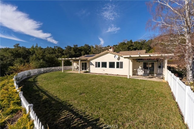 back of property with roof mounted solar panels, a patio area, a yard, and a fenced backyard