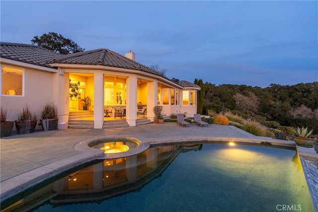 pool at dusk with a patio area, an outdoor pool, and an in ground hot tub