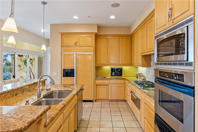 kitchen featuring hanging light fixtures, light stone countertops, appliances with stainless steel finishes, and a sink