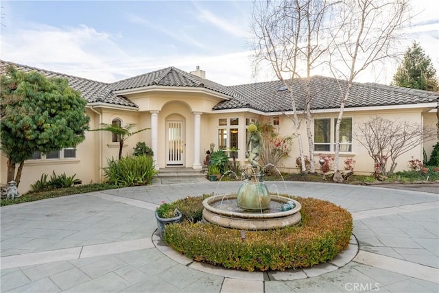 view of front facade with a tile roof, curved driveway, a chimney, and stucco siding