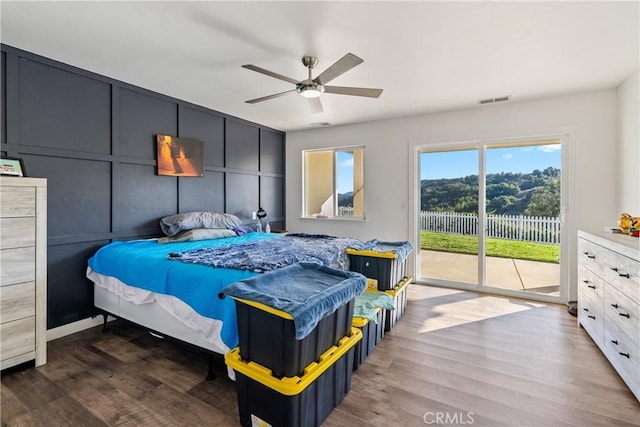 bedroom featuring access to outside, wood finished floors, visible vents, and a decorative wall