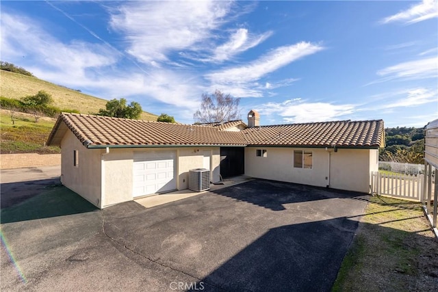 ranch-style house featuring a tile roof, a chimney, stucco siding, fence, and cooling unit