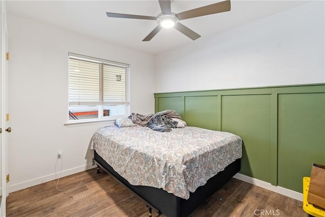 bedroom with ceiling fan, baseboards, wood finished floors, and a decorative wall