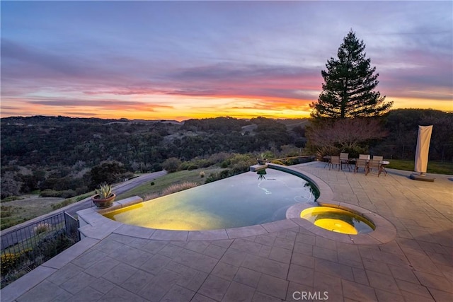 view of pool with a patio area, fence, an infinity pool, and an in ground hot tub