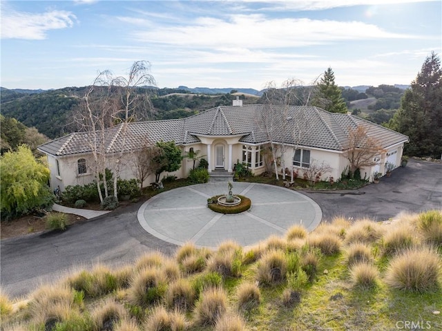 mediterranean / spanish house with stucco siding, a chimney, curved driveway, and a tiled roof